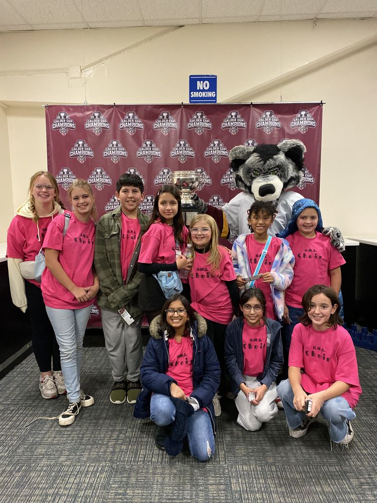 Ten choir students posing with Skates the Grey Wolf in front of a Chicago Wolves step and repeat