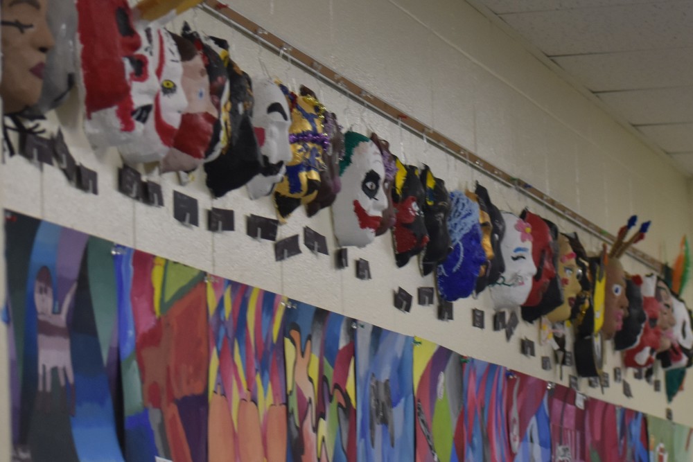 Student art projects hanging on the wall above lockers including masks and geometric prints