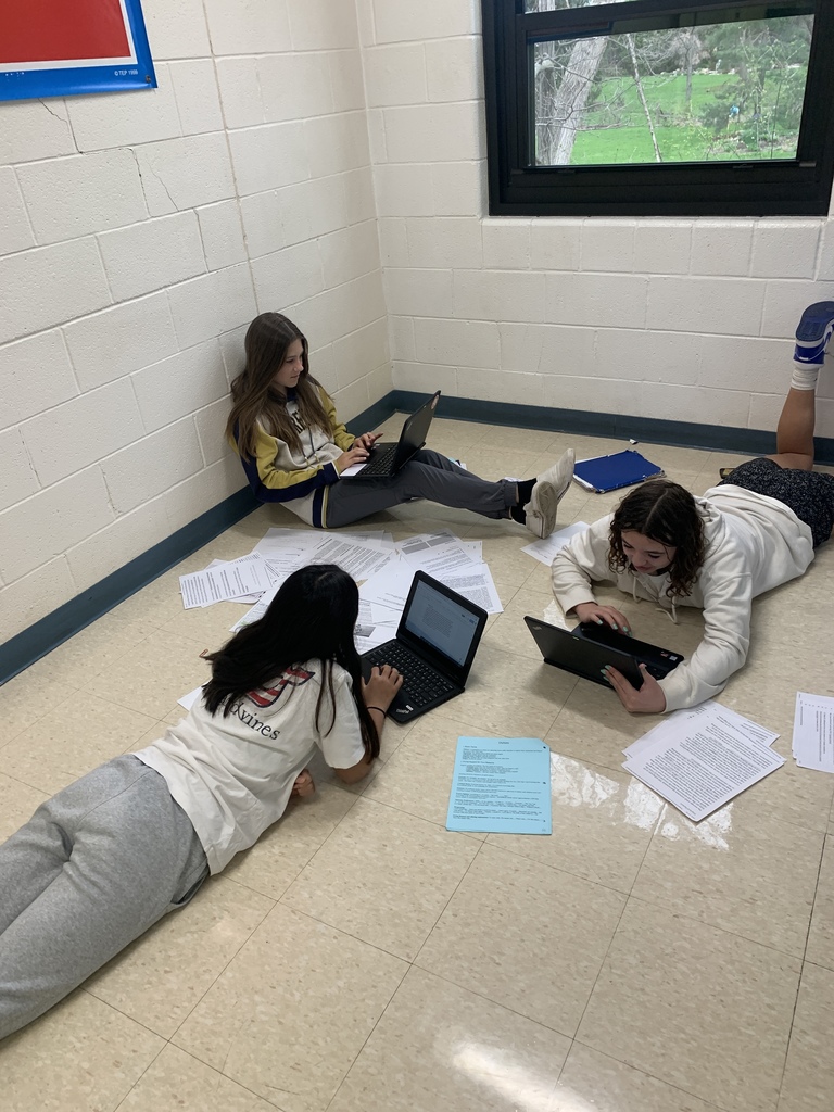 image 1: Three girls working on computers on the floor, one sitting against a wall, two laying on their stomachs; all three facing each other.  