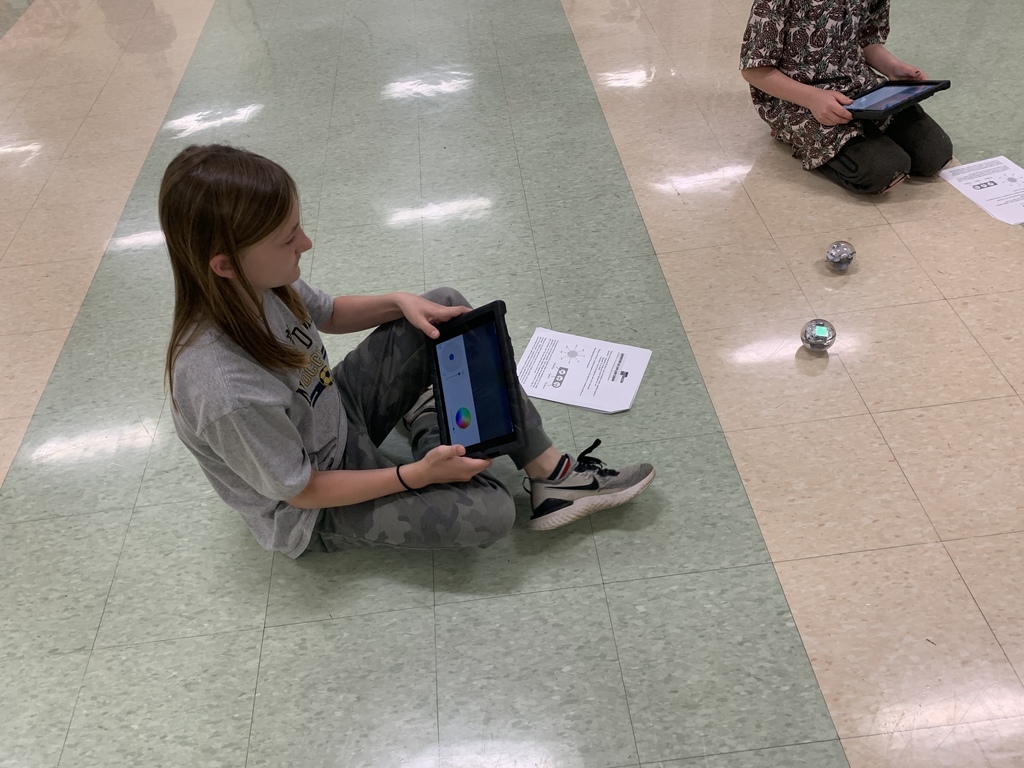 One student sitting on the floor holding an iPad with a Sphero in front of her.