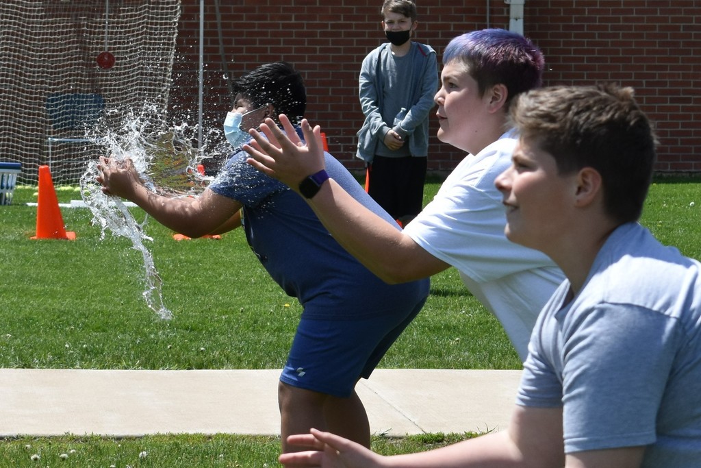 A water balloon explodes in one student's hands while two others wait for their water balloons to be thrown to them