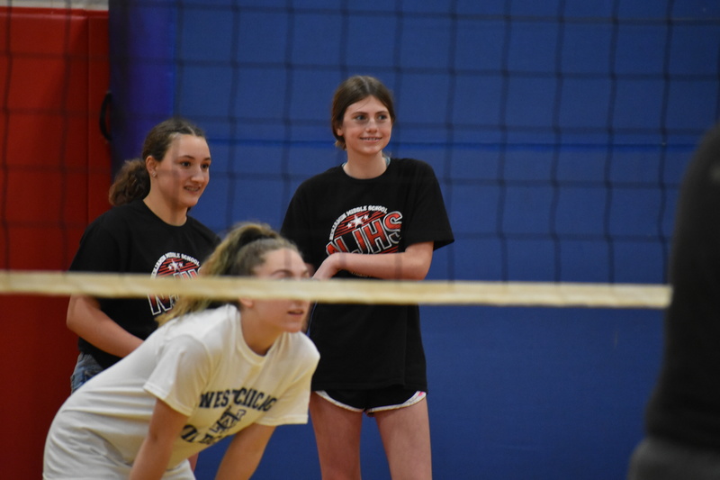 Three students smile as they get ready for the teacher serve during the Staff vs. Student volleyball game at Charity Fest